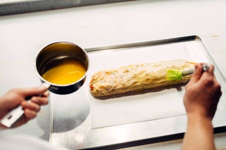 Chef hand lubricates strudel with egg and butter