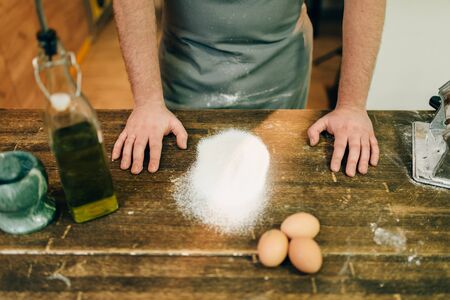 Male chef in apron, flour and eggs on wooden tableの写真素材