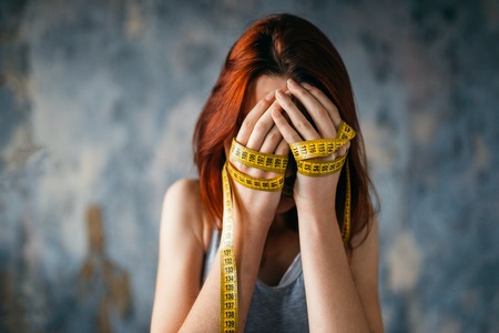 Woman covers face, hands tied with measuring tapeの写真素材