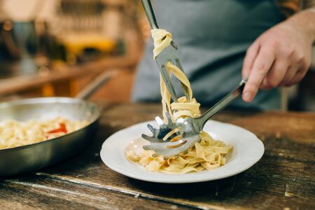 Male chef puts fresh pasta in a plateの写真素材
