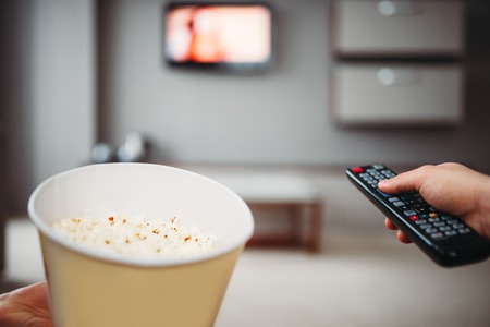 Male hands with tv remote control and popcorn