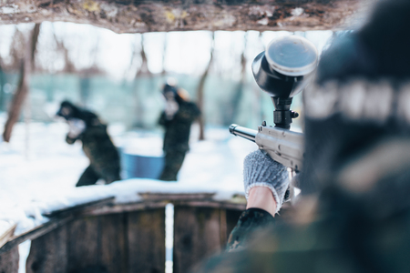 Paintball player shooting at the enemy team, winter forest battle. Extreme military gameの写真素材