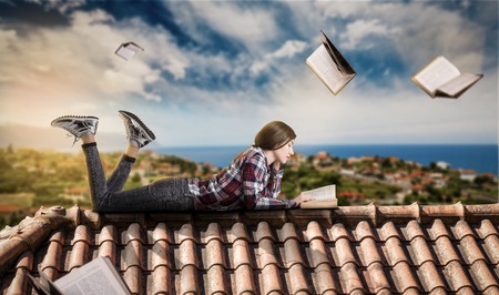 Woman reads while lying on the top of the roofの写真素材