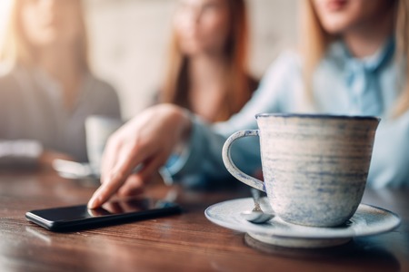 Cup of coffee and phone on wooden table, closeup