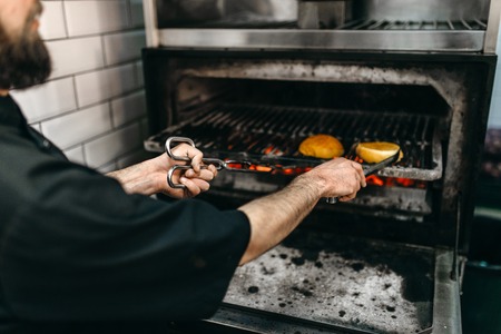 Male cook prepares tasty burger on grill ovenの写真素材