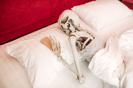 Human skeleton with phone in hand lies in bedの写真素材
