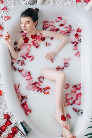 Sexy lady lying in bath with foam and rose petals