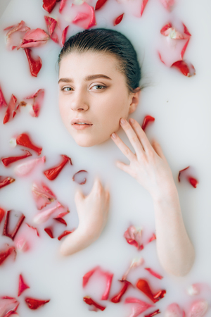 Woman face in the bath with foam and rose petalsの写真素材