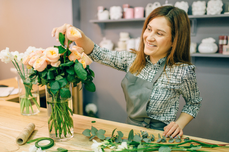 Florist puts fresh roses in a vase in flower shopの写真素材