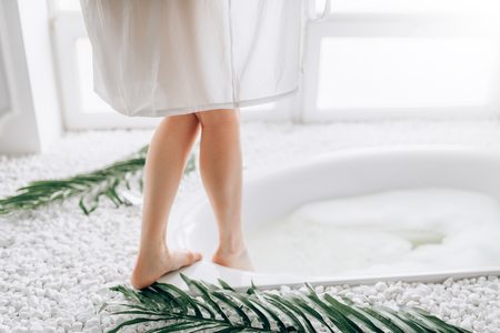 Woman in white bathrobe dips legs into the bathの写真素材