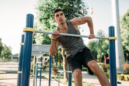 Athletic man doing exercise on horizontal bar on outdoor fitness workout. Strong sportsman on sport...