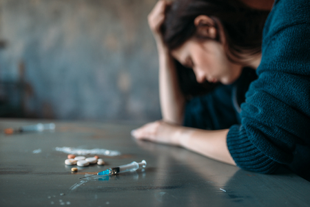 Drug addict sitting at the table with narcoticsの写真素材