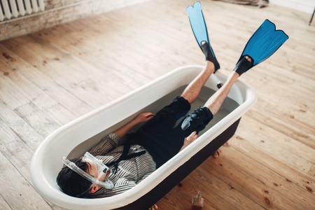 Businessman in flippers and mask lies in bathtubの写真素材