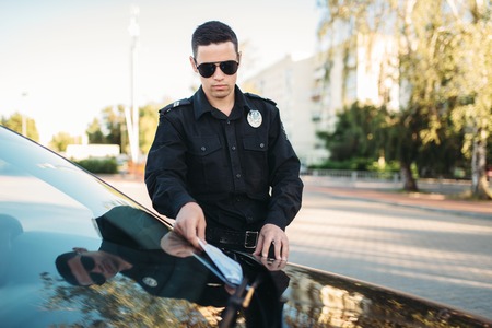 Male policeman in uniform writes a fine on roadの写真素材