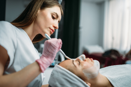 Doctor in gloves rubs the cream on patient faceの写真素材