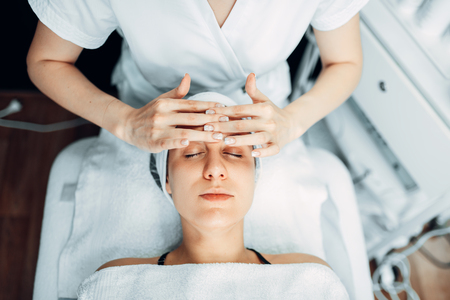 Beautician rubs the cream on female patient faceの写真素材