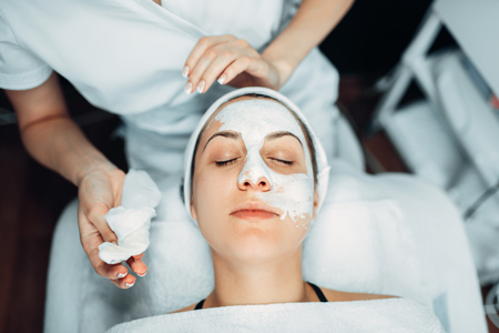Beautician hands with cream against patient faceの写真素材
