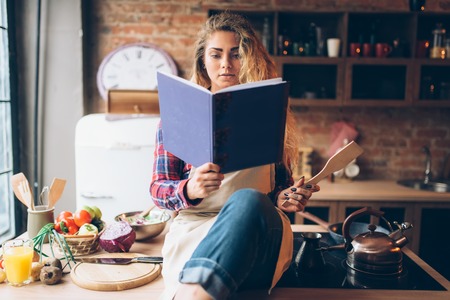 Young housewife in an apron reads recipe bookの写真素材