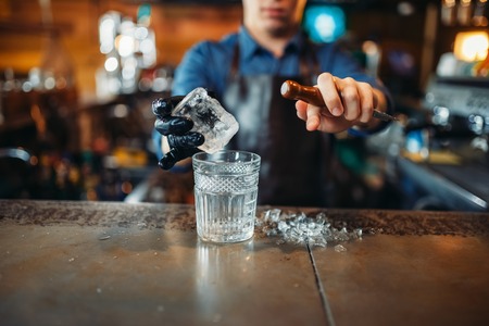 Male bartender pours a drink into a glass with iceの写真素材