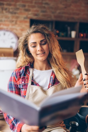 Young housewife in an apron reads recipe bookの写真素材