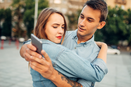 Man hugs woman and looking on gadget at this timeの写真素材