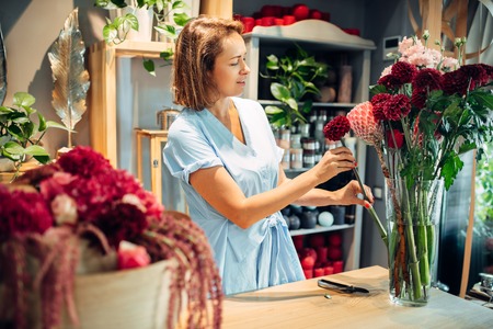 Female florist puts flowers in a vase, floral shopの写真素材