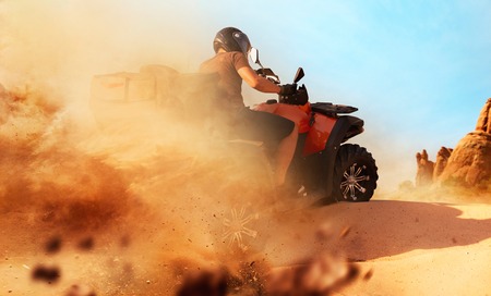 Atv riding in sand quarry, dust clouds. Male driver in helmet on quad bike, extreme freeriding on...