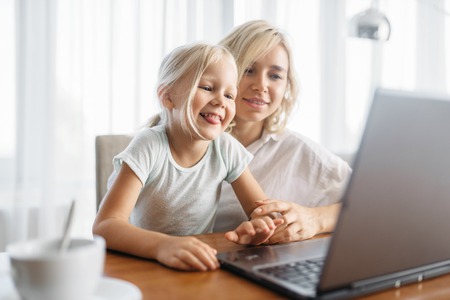 Smiling mother and child uses laptop at homeの写真素材