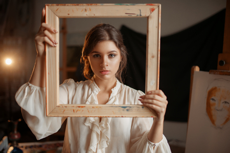 Female painter holds wooden frame at her faceの写真素材
