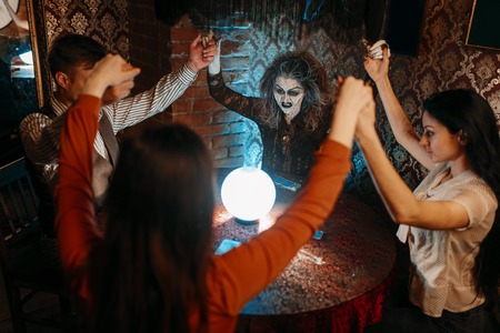 Witch over a crystal ball, young people on seance