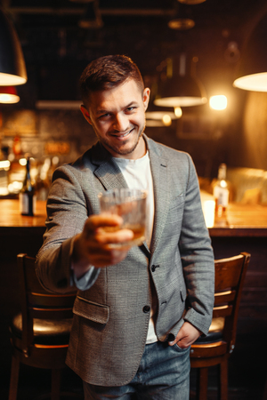 Smiling man stretches out glass of alcohol in barの写真素材