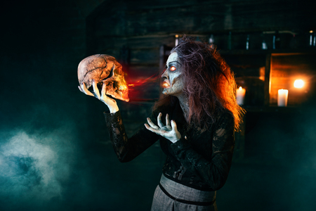 Scary witch holds human skull and reads the spellの写真素材