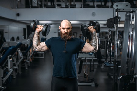 Muscular athlete poses with dumbbells in gym