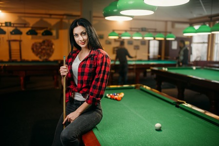 Female billiard player with cue poses at the table