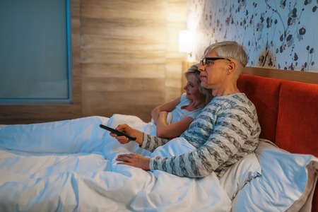 Mature love couple watching TV in bedroomの写真素材
