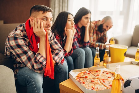 Sad friends watching TV at the boring house partyの写真素材