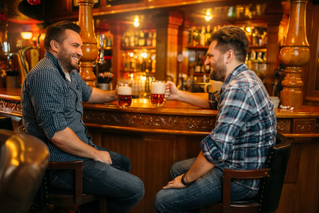 Two male friends drinks beer at the counter in pubの写真素材