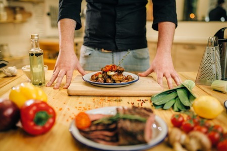 Plate wit roasted meat slices on wooden table, Male chef and fresh cooked dish for gourmets, kitchen on background. Man preparing beef with vegetables on countertopの写真素材