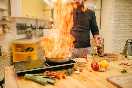 Male chef cooking meat with vetables on fire