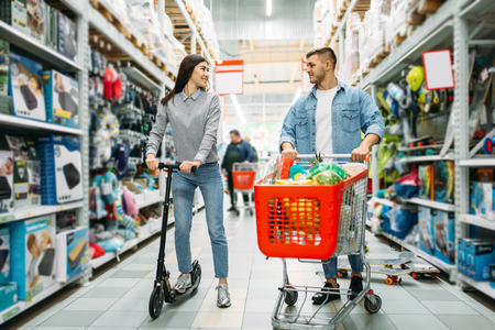 Couple in shop, husband with cart, wife on scooterの写真素材