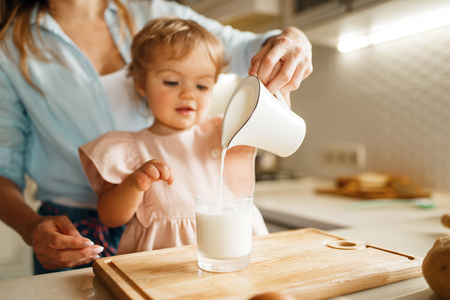 Young mother and kid pours milk into a glassの写真素材