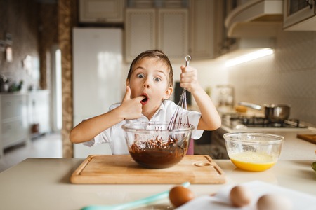 Male kid tastes melted chocolate in a bowlの写真素材