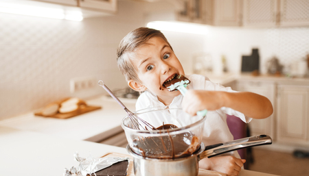 Young boy tastes melted chocolate in a bowlの写真素材