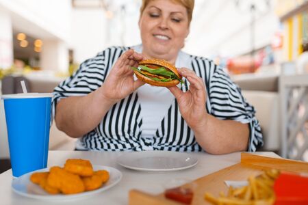 Fat woman eating fastfood in mall food courtの写真素材
