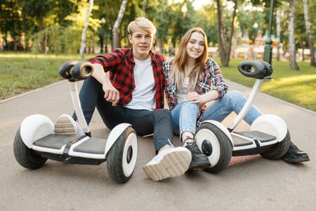 Young couple sitting on road with gyro board