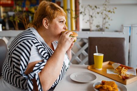 Fat woman eating burger in mall food courtの写真素材