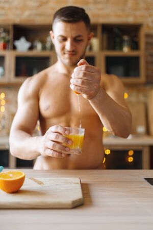 Muscular man with naked body cooking orange juice