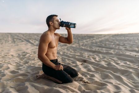 Male athlete drinks water after workout in desertの写真素材