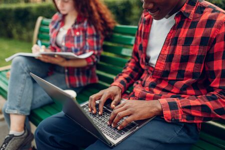 Two students studying on the bench in summer park