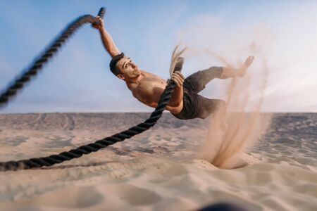 Male athlete with battle ropes, flying sand effectの写真素材
